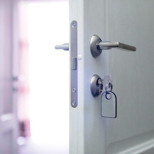 Door partially open with key inserted, welcoming light from hallway in home setting